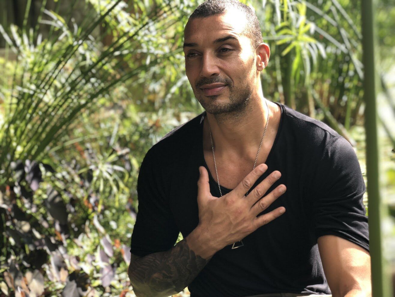 Alain among green plants, one hand resting on his heart